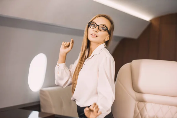 beautiful young girl in the cabin of a business class airplane with a phone in her hands comfortable luxury travel close to the porthole