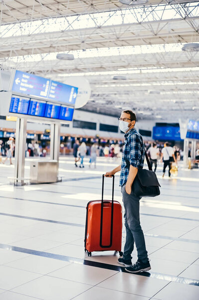 Airport european nerd man in glasses and plaid shirt with luggage tourist boarding plane taking a flight  wearing face mask. Coronavirus flu virus travel 