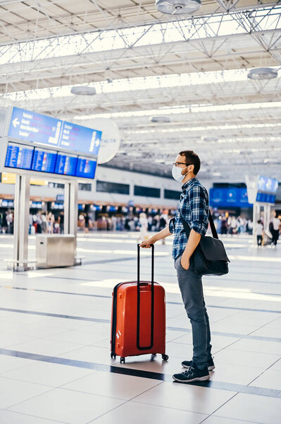 Европейский ботаник из аэропорта в очках и клетчатой рубашке с багажным туристическим самолетом, летящим в маске для лица. Вирусы коронавируса гриппа 