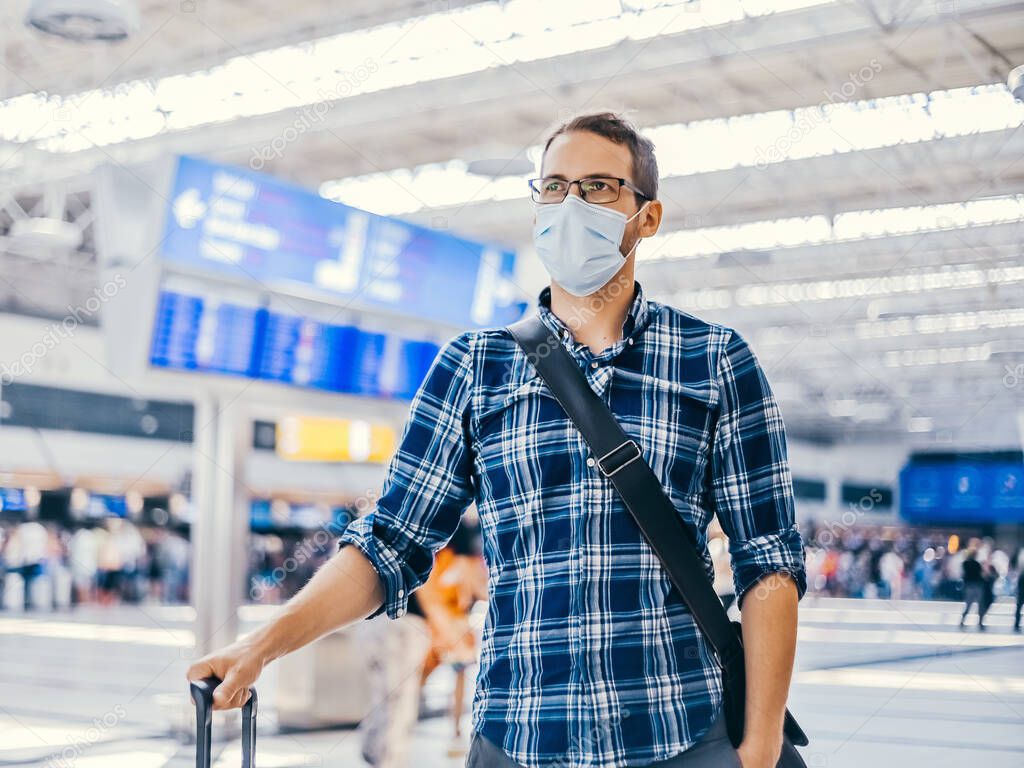 Airport european nerd man in glasses and plaid shirt with luggage tourist boarding plane taking a flight  wearing face mask. Coronavirus flu virus travel 