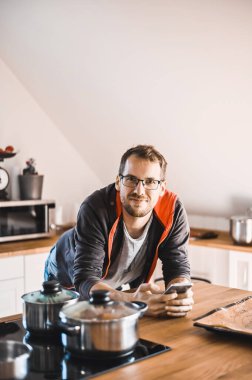 Şık bir mutfakta gözlüklü çekici inek telefonda tavuk tarifini takip ediyor.