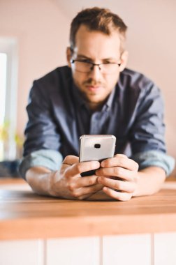 Şık mutfakta gözlüklü çekici inek bir adam ya tarifi takip ediyor ya da telefonda haber okuyor.