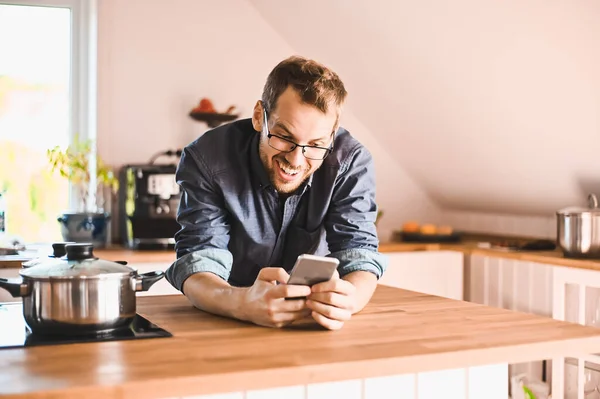 attractive nerd guy with glasses in stylish kitchen follows a recipe or  reads news on the phone