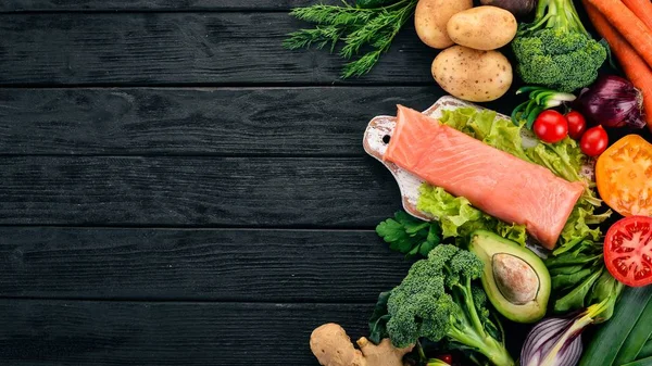 Salmon fillet and fresh vegetables. Healthy food. On a black wooden background. Healthy food. Top view. Copy space.