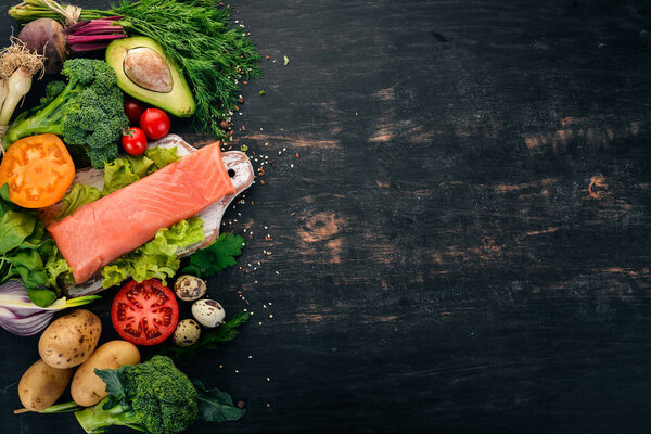 Salmon fillet and fresh vegetables. Healthy food. On a black wooden background. Healthy food. Top view. Copy space.