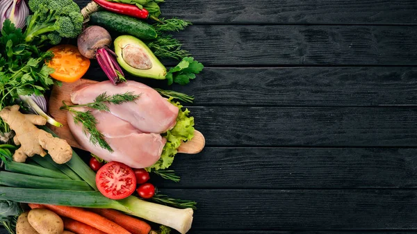 Chicken breast and fresh vegetables. Healthy food. On a black wooden background. Top view. Copy space.