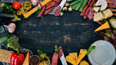 Sosis, peynir ve taze sebze ürün yelpazesine. İtalyan mutfağı. Siyah ahşap arka plan üzerinde. Üstten görünüm. Kopya alanı.