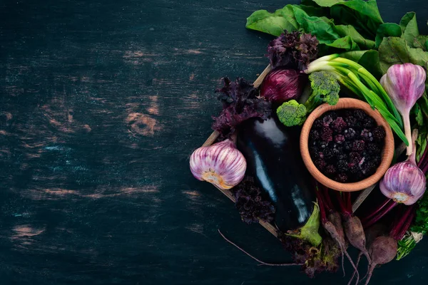 Purple food. Fresh vegetables and berries in a wooden box. On a wooden background. Top view. Copy space.