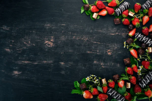 Strawberry with chocolate and candy. On a black wooden background. Top view. Copy space.