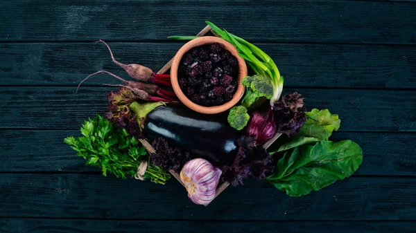 Purple food. Fresh vegetables and berries in a wooden box. On a wooden background. Top view. Copy space.