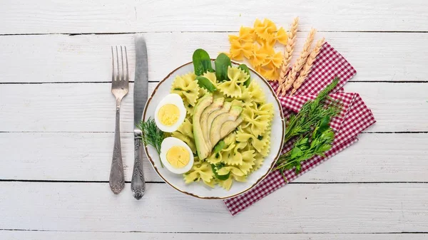 Pasta with spinach, avocado and boiled egg. On a wooden background. Top view. Copy space.