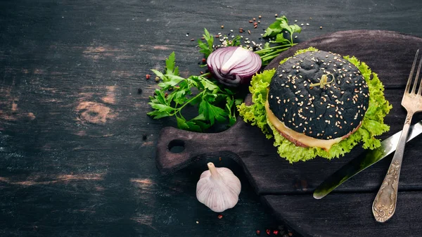 Black burger with meat, onion and lettuce. On a wooden background. Top view. Copy space.