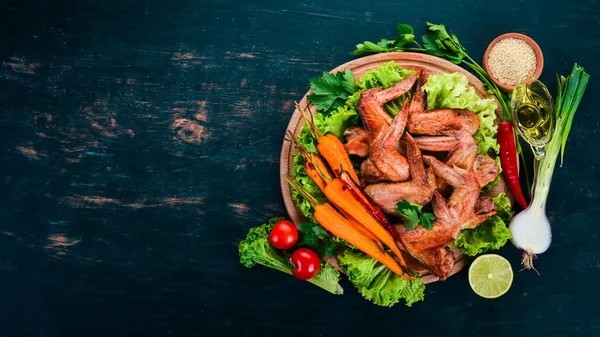 Sebze ve havuç ile ızgara tavuk kanatları. Ahşap bir arka plan üzerinde. Üstten görünüm. Kopya alanı.