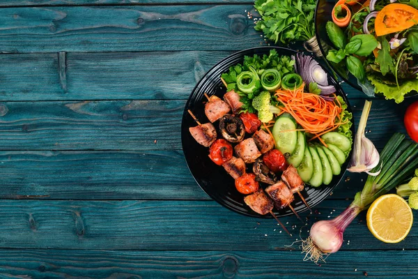 Bir tabak taze sebze ile pişmiş dana eti şiş kebap. Ahşap bir arka plan üzerinde. Üstten görünüm. Kopya alanı.