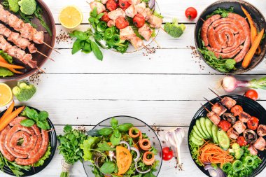 Barbekü et kümesi. Sosis, şiş, taze sebze. Domates, soğan, sarımsak. Beyaz ahşap zemin üzerinde. Kopya alanı.