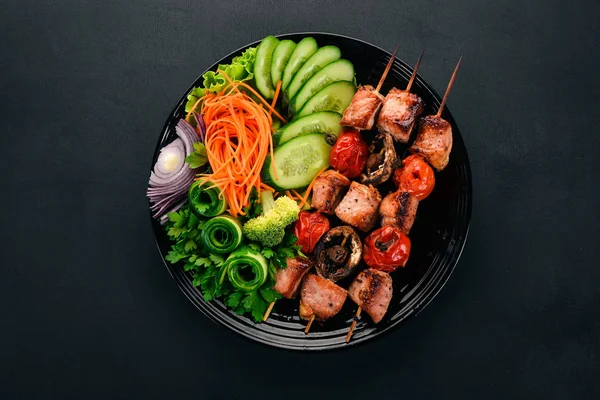 Baked veal shish kebab on a plate with fresh vegetables. On a wooden background. Top view. Copy space.