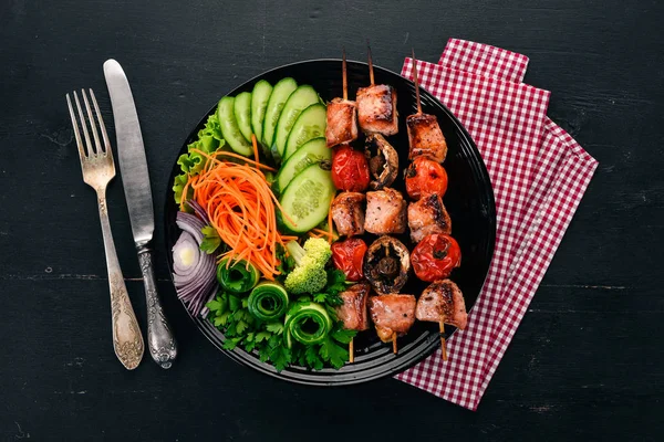Baked veal shish kebab on a plate with fresh vegetables. On a wooden background. Top view. Copy space.