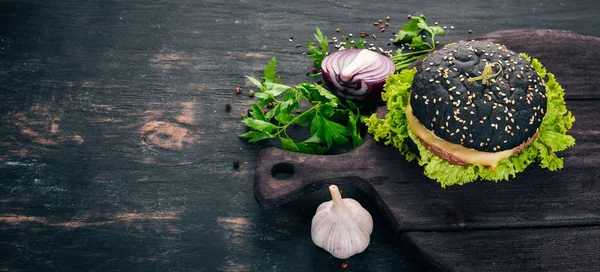 Black burger with meat, onion and lettuce. On a wooden background. Top view. Copy space.