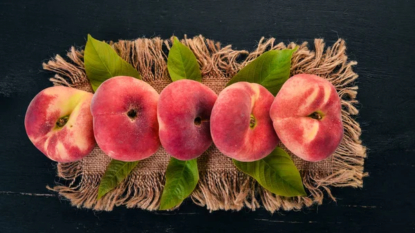 Flat peach with green leaves On a black wooden background. Top view. Free space for your text.