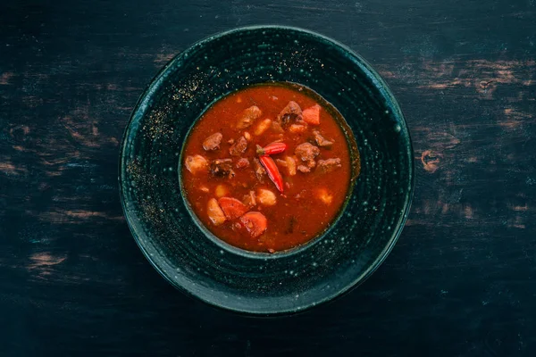 Tomato soup with beef and chili peppers in chervrniy plate. On a wooden table. Top view. Copy space. — Stock Image Tomato Soup Beef Chili Peppers Chervrniy Plate Wooden Table Top Stock Image
