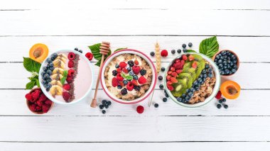 Yulaf lapası meyve ve çilek ile geniş ürün yelpazesine. Kahvaltı. Beyaz ahşap zemin üzerinde. Üstten görünüm. Metin için boş alan.