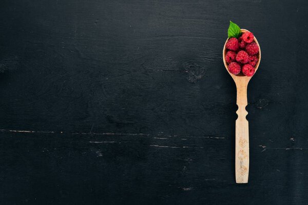 Raspberry berries in a wooden spoon. On a wooden background. Top view. Free space for your text.