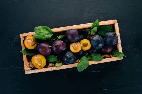 Plums with leaves in a wooden box. On a black wooden background. Top view. Free space for your text.