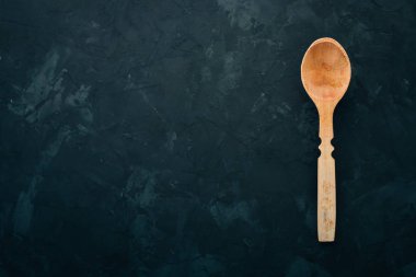 Siyah bir taş zemin üzerine tahta kaşık. Üstten görünüm. Metin için boş alan.