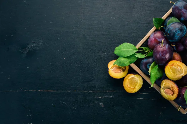 Plums with leaves in a wooden box. On a black wooden background. Top view. Free space for your text.