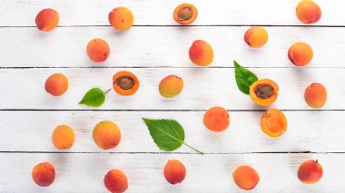 Beyaz ahşap zemin üzerinde yaprakları ile taze kayısı. Üstten görünüm. Metniniz için boş alan.