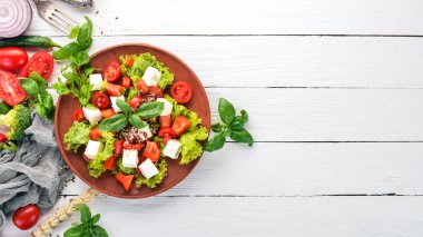 Bir tabak salata. Beyaz peynir, kiraz domates, kırmızı biber, marul. Sağlıklı gıda. Beyaz ahşap masa masaya. Üstten görünüm. Metin için boş alan.