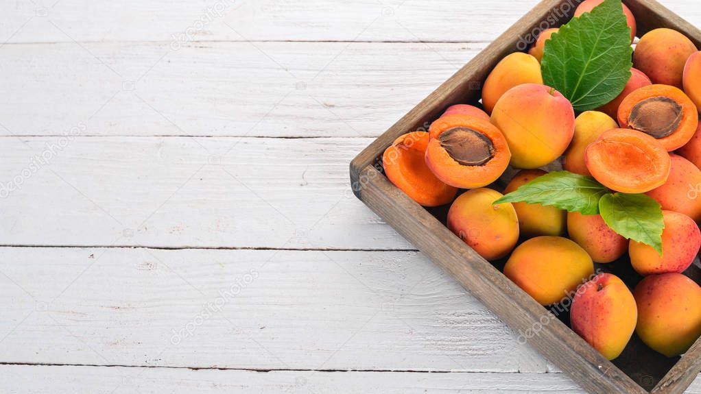 Apricots in a wooden box. Fresh fruits. On a white wooden background. Top view. Free space for your text.