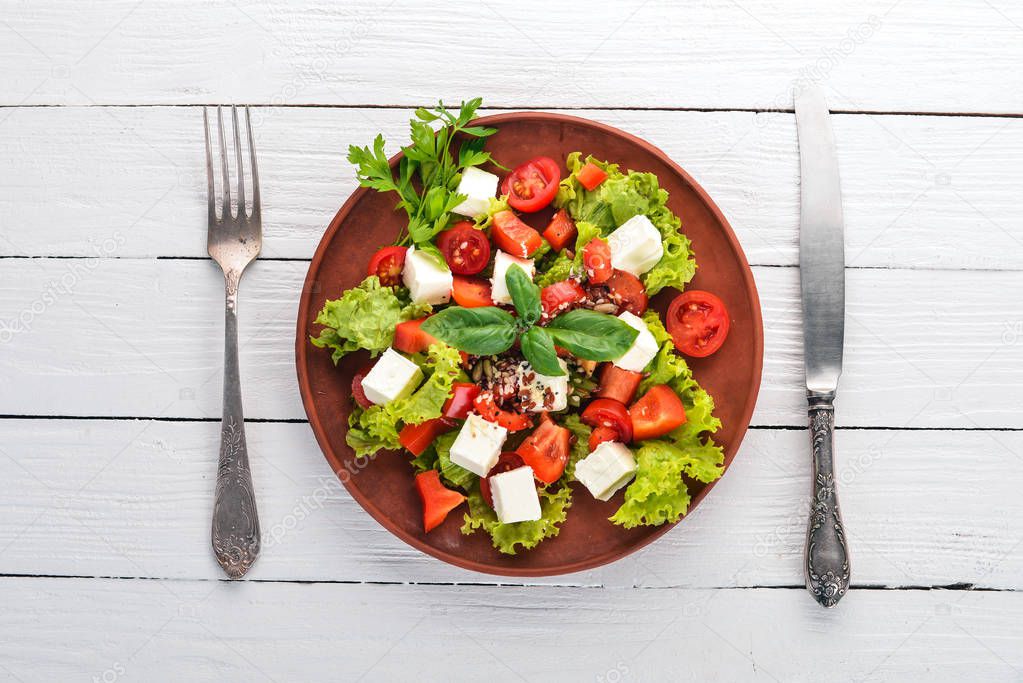 Salad in a plate. Feta cheese, cherry tomatoes, paprika, lettuce. Healthy food. On a white wooden table table. Top view. Free space for text.