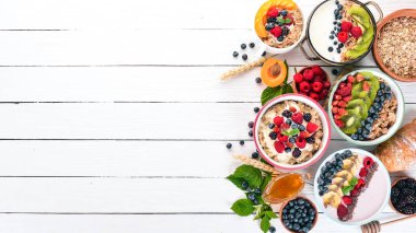 Yulaf lapası meyve ve çilek ile geniş ürün yelpazesine. Kahvaltı. Beyaz ahşap zemin üzerinde. Üstten görünüm. Metin için boş alan.