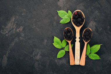 Taze böğürtlen içinde bir kaşık. Siyah taş arka plan üzerinde. Üstten görünüm. Metin için boş alan.