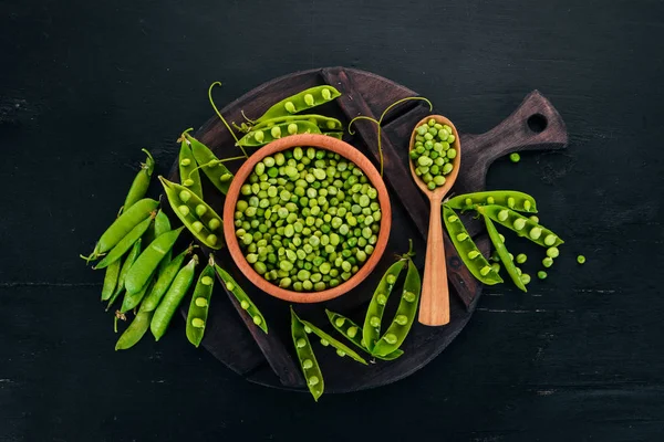 Green peas in a wooden plate. On a wooden background. Top view. Free space for your text.