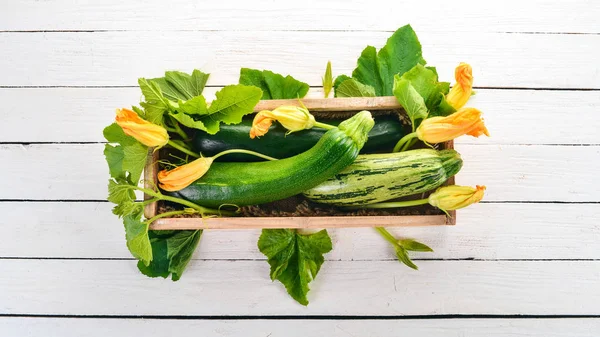 Green zucchini in a wooden box. Fresh vegetables. On a white wooden background. Top view. Copy space.