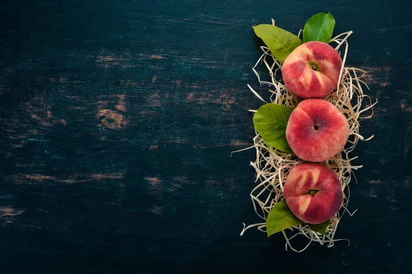 Platte Perzik Met Groene Bladeren Een Zwarte Houten Achtergrond Bovenaanzicht — Stockfoto