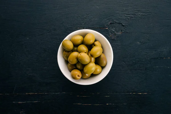 Green olives in a plate.On a black wooden background. Free space for text.