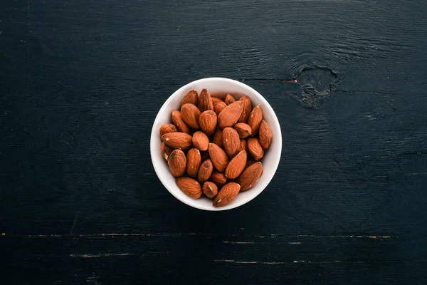 Almonds in a plate. On a black wooden background. Free space for text.