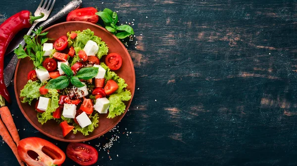 Bir tabak salata. Beyaz peynir, kiraz domates, kırmızı biber, marul. Sağlıklı gıda. Siyah ahşap masa masaya. Üstten görünüm. Metin için boş alan.