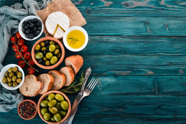 A set of green olives and black olives, and snacks. On a blue wooden table. Free space for text.
