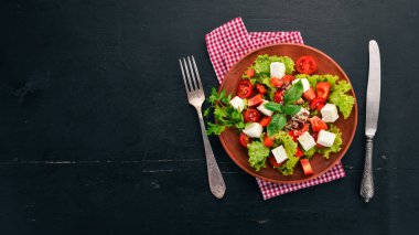 Bir tabak salata. Beyaz peynir, kiraz domates, kırmızı biber, marul. Sağlıklı gıda. Siyah ahşap masa masaya. Üstten görünüm. Metin için boş alan.