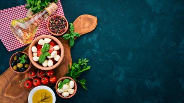 Bir caprese salatası yemek. Mozzarella peyniri, domates, zeytin, fesleğen yaprağı, yağ, karabiber. Siyah taş masanın üstünde. Metin için boş alan.