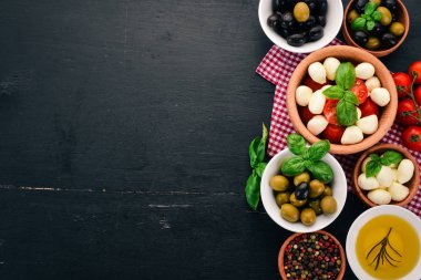 İtalyan caprese salatası için malzemeler. Mozzarella peyniri, kiraz domates, fesleğen yaprağı, zeytin, yağ, karabiber. Siyah ahşap arka plan üzerinde. Metin için boş alan.