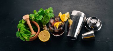 Viski, limon ve nane alkollü kokteyl. Rom-kola. Brandy. Siyah ahşap arka plan üzerinde. Metin için boş alan.