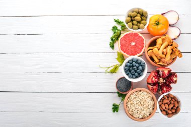 Beyaz ahşap bir masa üzerinde sağlıklı gıda. Taze sebze, meyve, fındık, çilek, mantar. Üstten görünüm. Metin için boş alan.