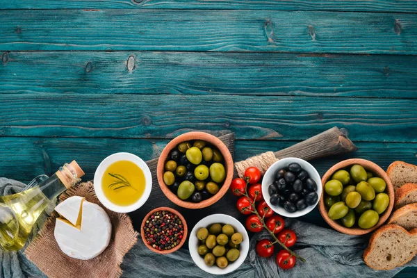 A set of green olives and black olives, and snacks. On a blue wooden table. Free space for text.