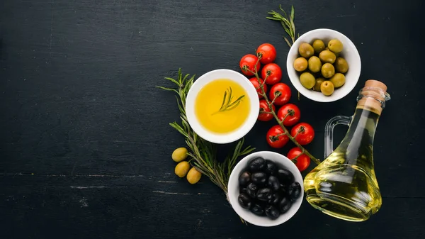 Olives, olive oil, cheese and spices. On a black wooden background. Free space for text.