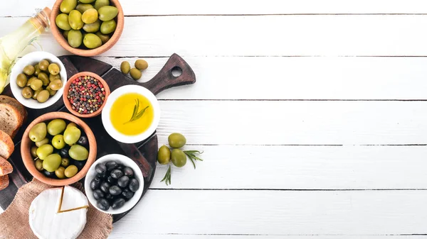 Green olives and black olives, oil, bread, cheese and snacks. Italian cuisine. On a white wooden table. Top view. Free space for text.